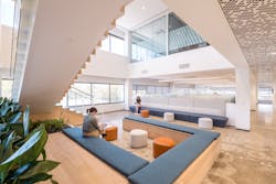 Double-height spaces with open stairs are filled with natural light and designed to encourage gathering. A glass-walled conference room overlooks a lounge area.