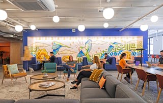 A co-working lounge on the third floor is anchored by a bird mural, highlighted by LED strip lighting. Classic globe lights are Luna Cord Pendant fixtures from Schoolhouse.